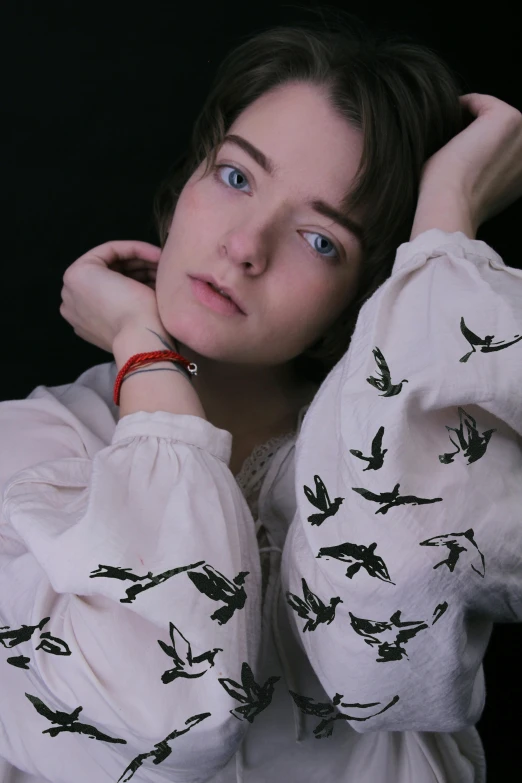 a woman wearing a white shirt with black birds on it, an album cover, inspired by Anna Füssli, trending on pexels, maisie williams, pale fair skin!!, colored photo, ((portrait))