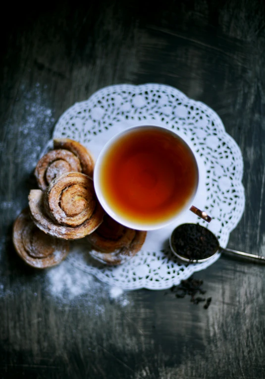 a cup of tea and some pastries on a table, inspired by Wlodzimierz Tetmajer, trending on unsplash, romanticism, intricate spirals, square, rosette, smoky