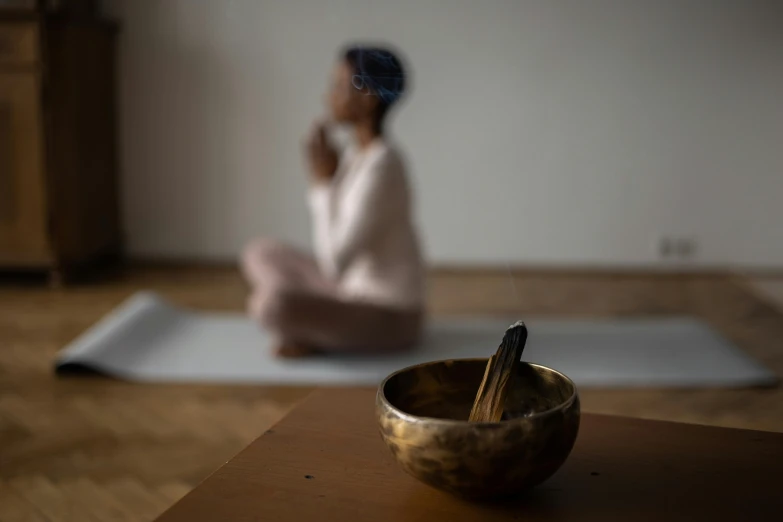 a woman sitting on a yoga mat talking on a cell phone, by Emma Andijewska, pexels contest winner, light and space, wooden bowl, incense, slightly out of focus, low quality photo