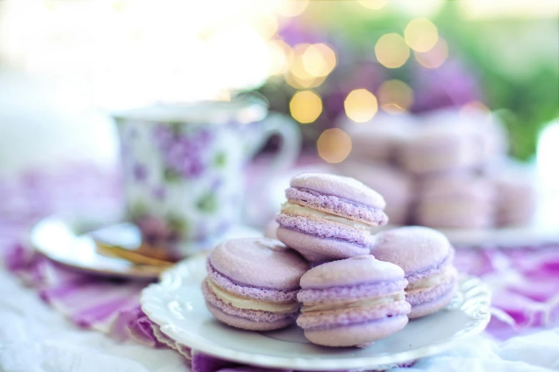 a white plate topped with purple macarons next to a cup of coffee, pexels contest winner, rococo, background image, cakes, dazzling lights, purple tint