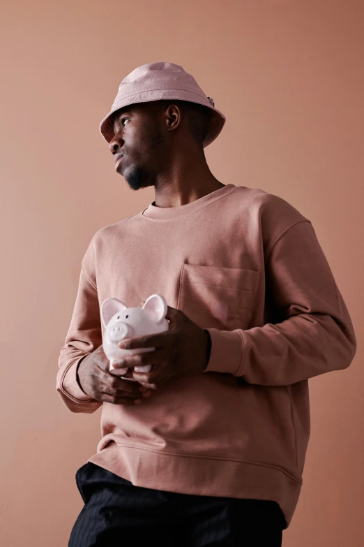 a man standing in front of a brown wall, wearing a pastel pink hoodie, cat with a hat, 2019 trending photo, piglet