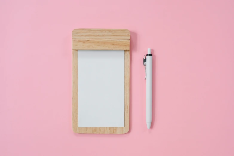 a notepad with a pen next to it on a pink surface, made of wood, product image, whiteboard, no type