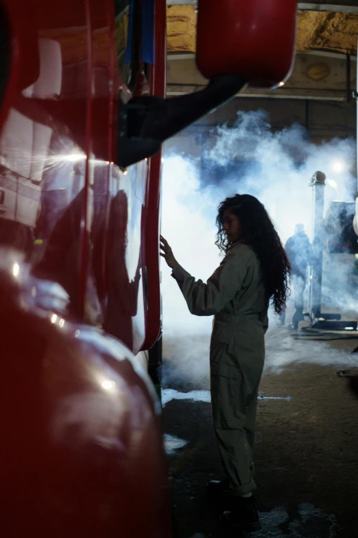 a woman standing next to a fire truck with smoke coming out of it, inspired by Bruce Davidson, pexels contest winner, arbeitsrat für kunst, she is in the potions workshop, aida muluneh, still from a terence malik film, welding torches for arms