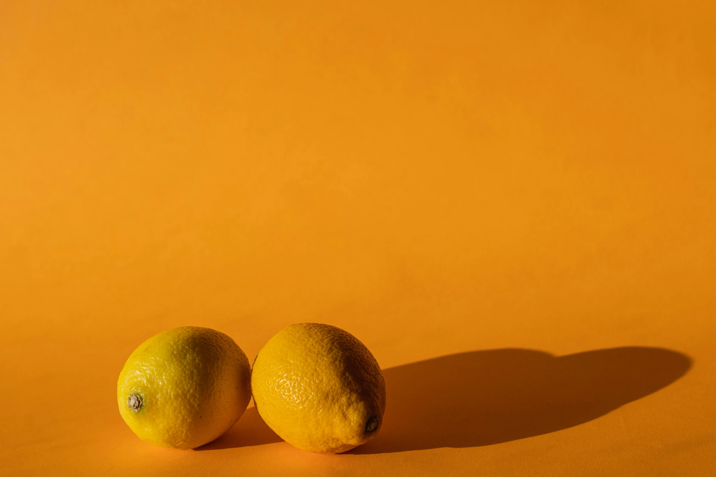 two lemons sitting next to each other on a yellow surface, by Andries Stock, unsplash contest winner, background image, orange light, full body image, thumbnail