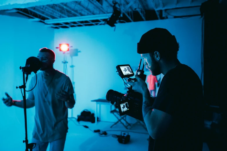 a couple of men standing next to each other in a room, pexels contest winner, video art, cinematic blue lighting, behind the scenes photo, performing a music video, shot with a professional camera