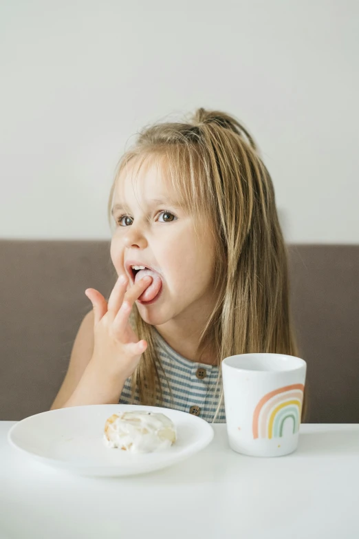 a little girl sitting at a table with a plate of food, licking out, high quality product image”, vanilla, detail shot