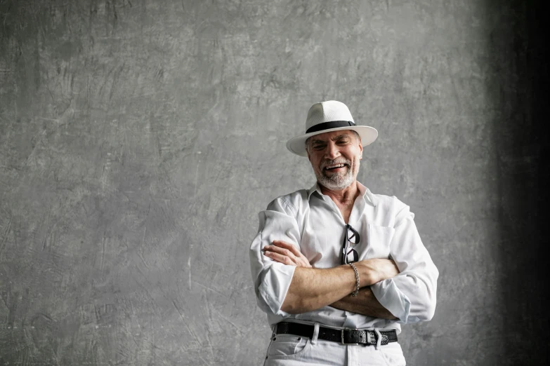 a man in a hat standing with his arms crossed, inspired by Agustín Fernández, pexels contest winner, short white beard, confident relaxed pose, white trendy clothes, white and grey