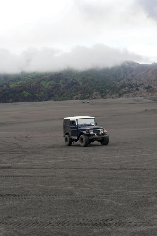 a jeep driving through the desert on a cloudy day, sumatraism, flowing lava and ash piles, square, black sand, brown