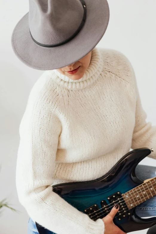 a woman in a hat playing a guitar, inspired by Tex Avery, trending on pexels, grey sweater, in white turtleneck shirt, non binary model, detailed product shot