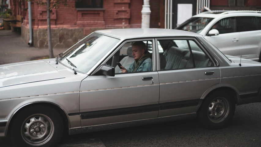 a man driving a silver car down a street, inspired by Elsa Bleda, unsplash, renaissance, humans of new york style, bmw e 3 0, moskvich, ignant