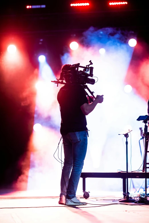 a man standing on a stage holding a video camera, pexels, happening, concert lights, tv still, instrument, backfacing