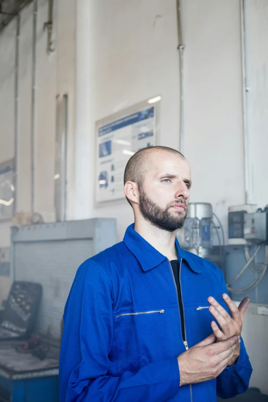 a man standing in front of a machine in a factory, inspired by Jakub Husnik, unsplash, arbeitsrat für kunst, wearing blue jacket, looking left, demna gvasalia, white metal