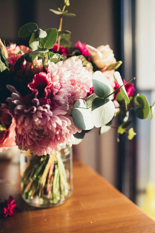 a vase filled with flowers sitting on top of a wooden table, by Elsie Few, trending on unsplash, romanticism, soft natural light, pinks, vibrant foliage, flower shop scene