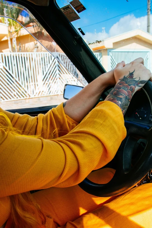 a woman sitting in the driver's seat of a car, a tattoo, inspired by Elsa Bleda, wearing a yellow hoodie, panoramic shot, 2019 trending photo, justina blakeney