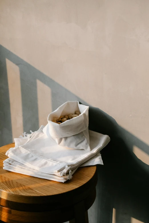 a bowl of cereal sitting on top of a wooden table, a still life, trending on unsplash, light and space, white cloth in wind shining, bags, bao phan, shadows