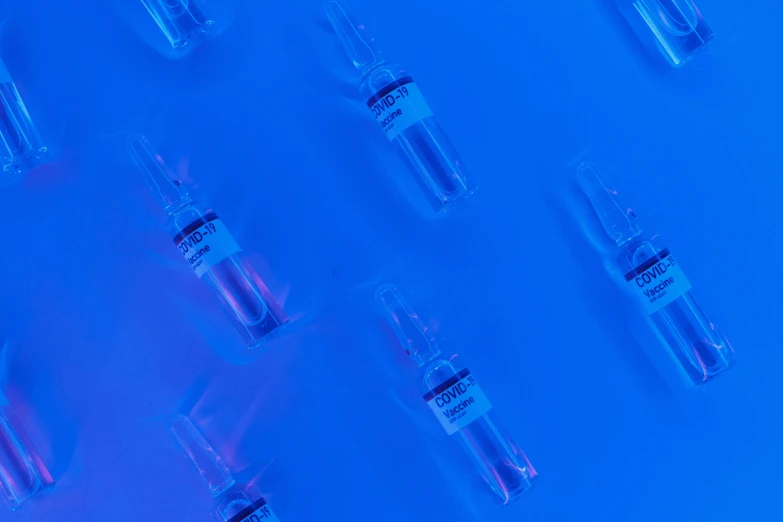 a group of vials sitting on top of a blue surface, blue neon accents, background image, syringe, thumbnail