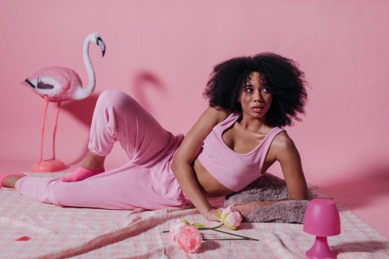 a woman laying on top of a bed next to a pink flamingo, by Jessie Alexandra Dick, trending on pexels, wearing a tracksuit, with afro, various posed, alex heywood