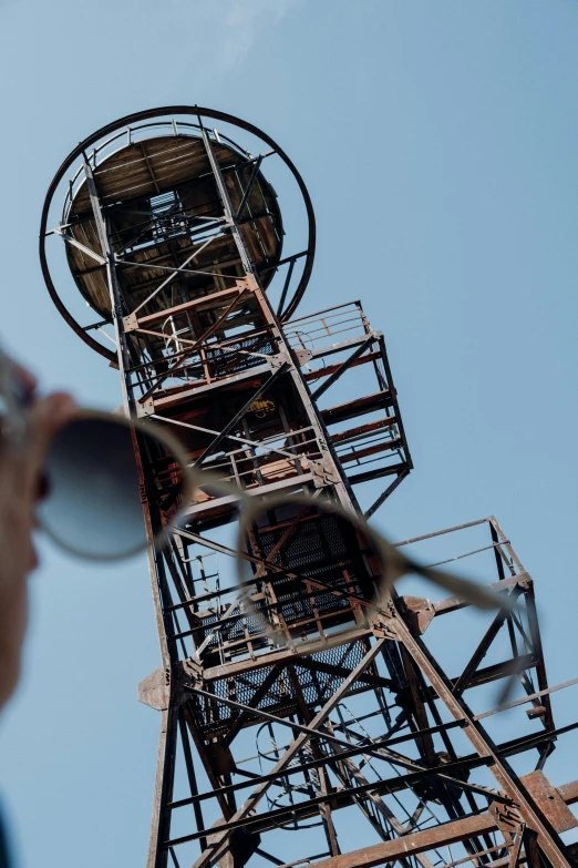 a man standing in front of a tall tower, a portrait, unsplash, dada, scrapyard architecture, big monocular, ((rust)), low detail