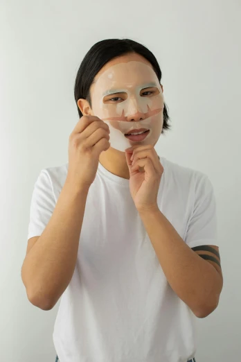 a woman putting a facial mask on her face, by Julia Pishtar, wearing translucent sheet, asian male, on clear background, silicone skin