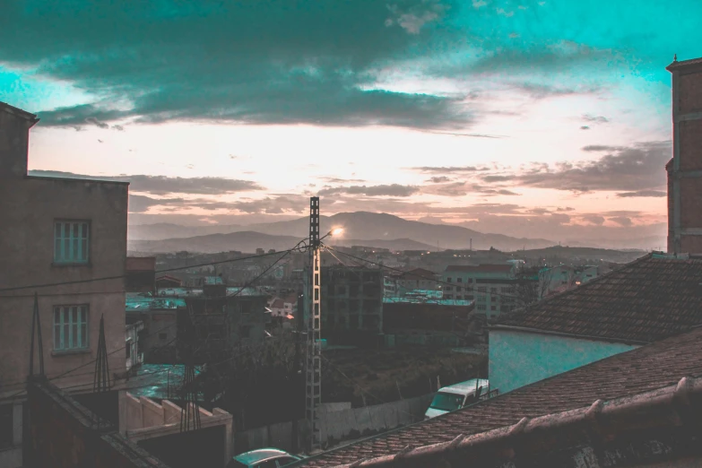 a view of a city from the top of a building, pexels contest winner, renaissance, teal sky, moody sunset in background, hills in the background, post grunge