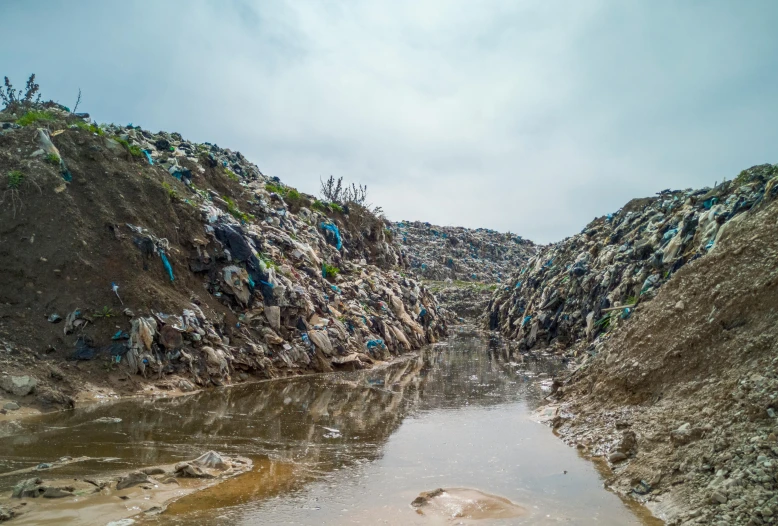 a body of water sitting next to a pile of garbage, unsplash, multiple stories, muddy embankment, terraformation, múseca illil