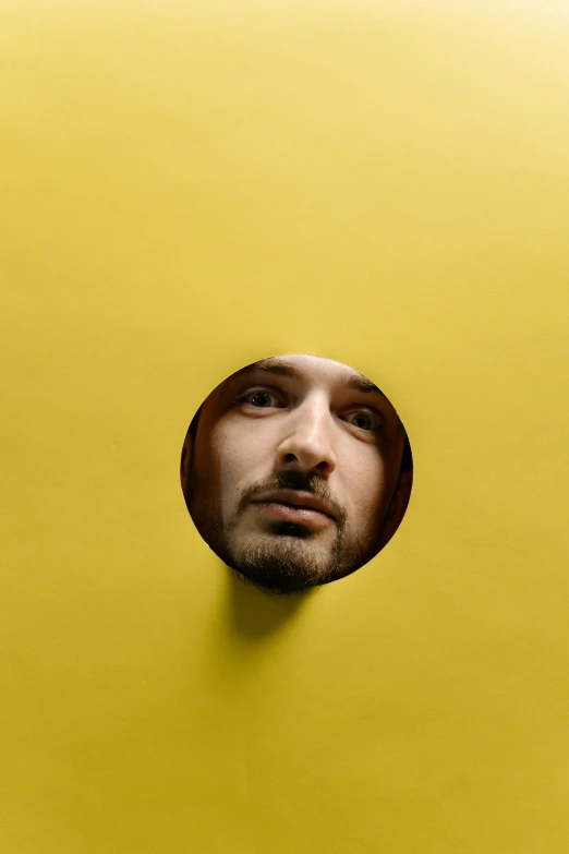 a man looking through a hole in a yellow wall, an album cover, reddit, conceptual art, shia labeouf, portrait mode photo, round - face, studio photo