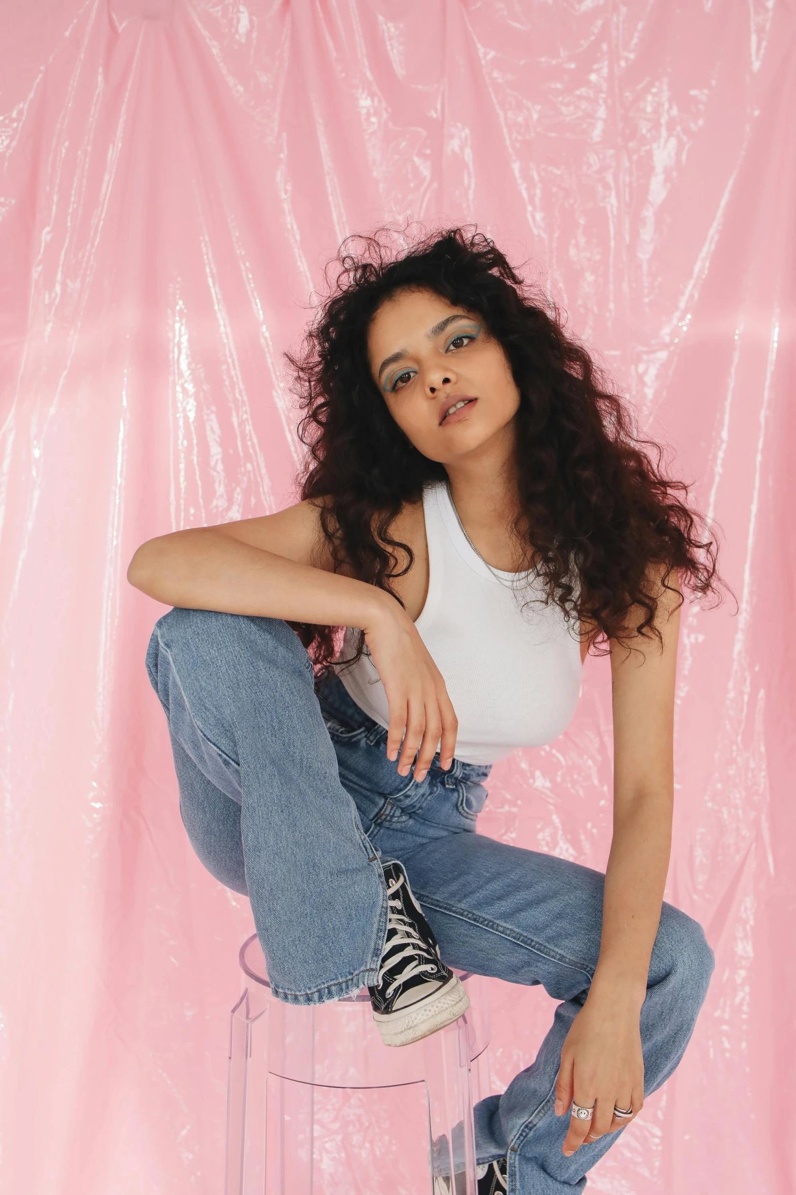 a woman sitting on top of a clear stool, an album cover, featured on instagram, renaissance, baggy jeans, (dark shorter curly hair), at a fashion shoot, asher duran