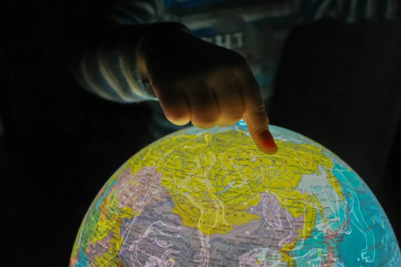 a close up of a person pointing at a globe, by Daniel Lieske, pexels, interactive art, nightlight, little kid, cartographic, modeled