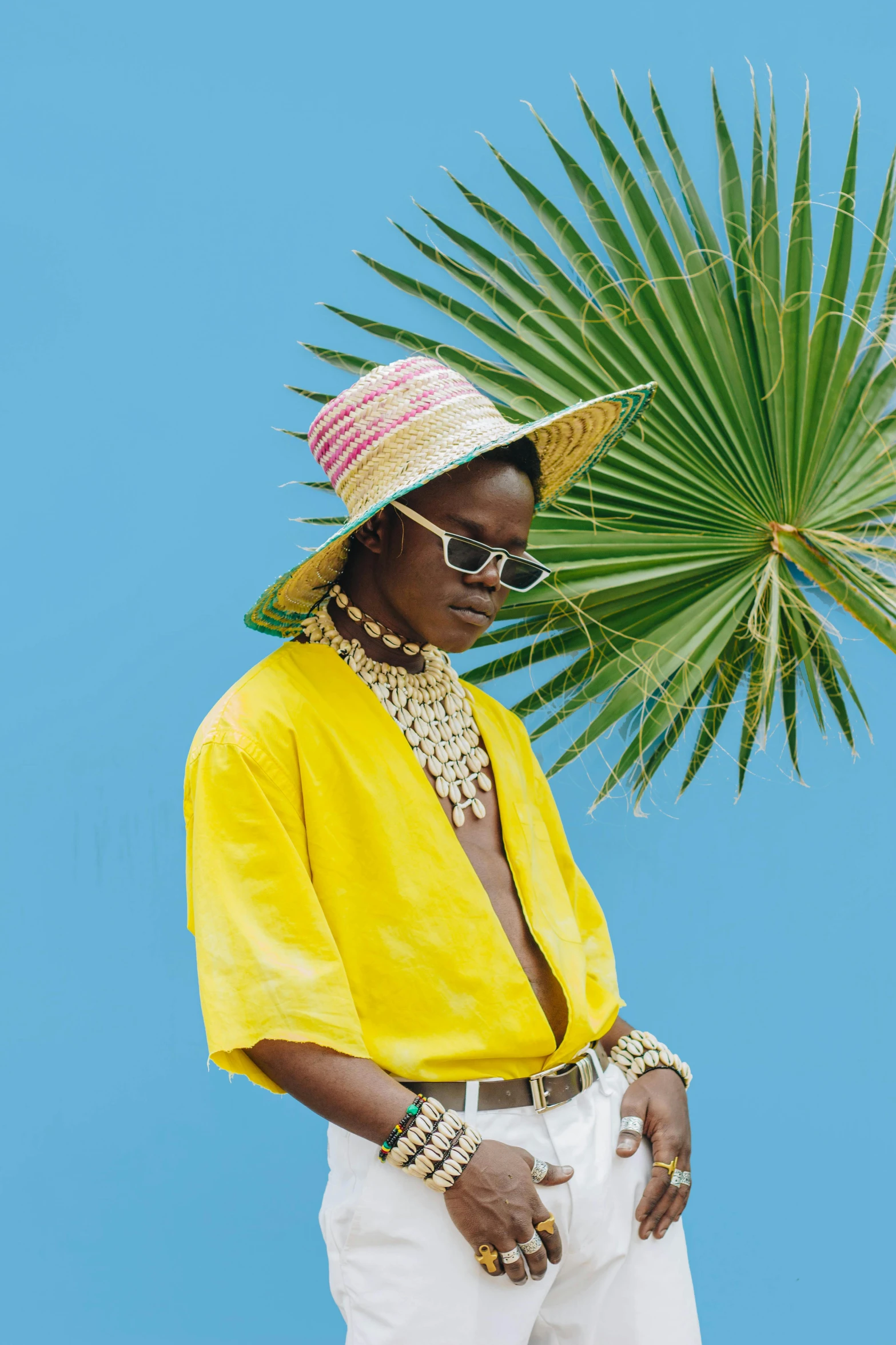 a man standing in front of a palm tree, an album cover, trending on pexels, maximalism, yellow clothes, maria borges, wearing sombrero, young thug