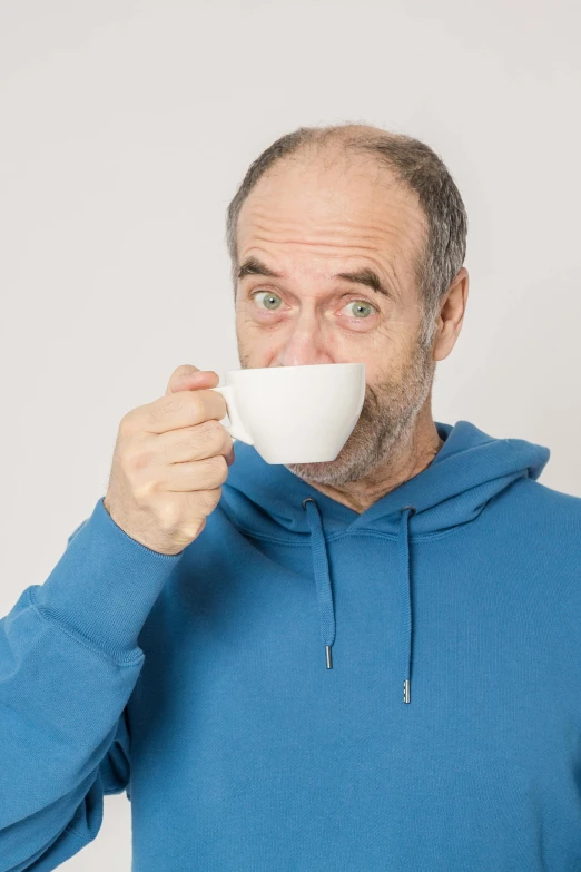 a man in a blue hoodie drinking from a white cup, by Matthias Stom, pexels contest winner, photorealism, jerry seinfeld, grumpy [ old ], 2 5 6 x 2 5 6 pixels, tea