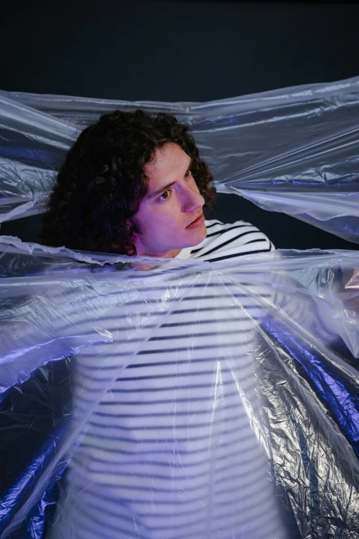 a woman laying on a bed covered in plastic, an album cover, inspired by Christo, unsplash, finn wolfhard, tubular creature, in a claustrophobic, lgbtq