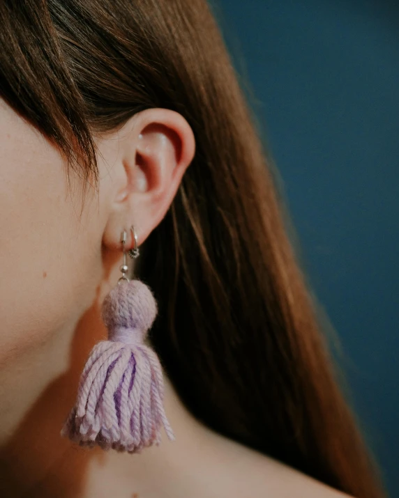 a close up of a woman wearing a pair of earrings, by Helen Stevenson, light purple, tassels, queer woman, close-up product photo