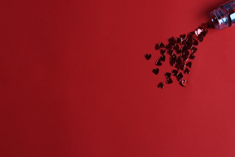 a bottle of water sitting on top of a red surface, falling hearts, dark red and black color palette, beads, background image