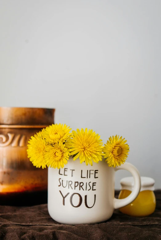 a vase filled with yellow flowers sitting on top of a table, inspired by Leo Leuppi, unsplash, happening, white mug, dandelion, hidden message, super close up shot