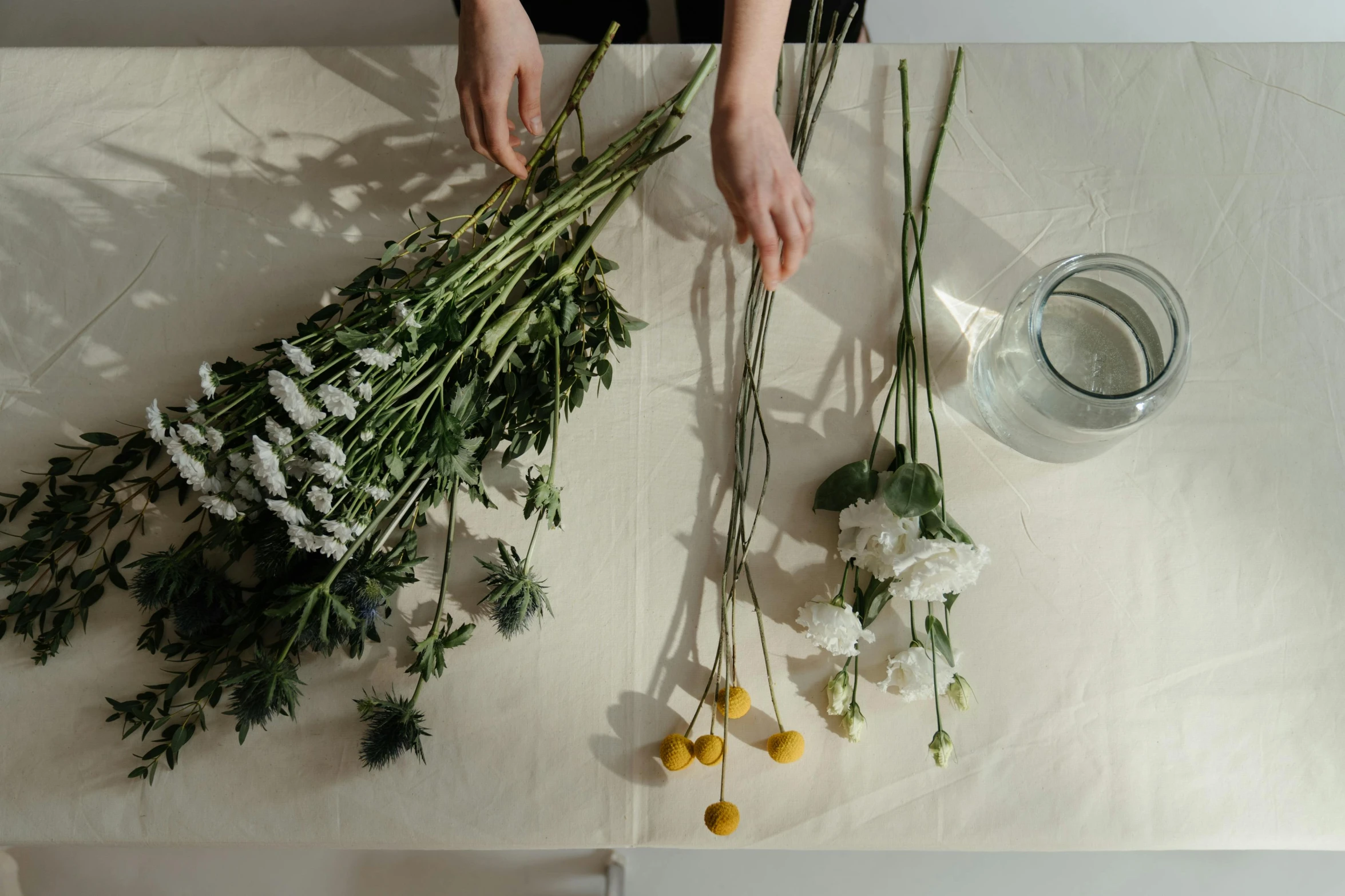 a person holding a bunch of flowers on a table, a still life, unsplash, process art, white and yellow scheme, stems, ignant, ingredients on the table
