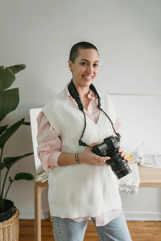 a woman standing in a room holding a camera, dasha taran, profile image, medical photography, smiling at camera