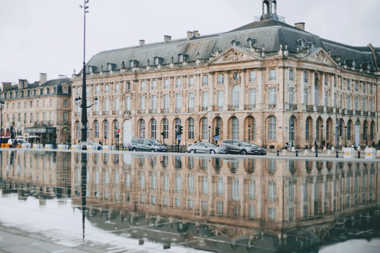 a reflection of a building in a puddle of water, by Raphaël Collin, pexels contest winner, neoclassicism, square, unsplash 4k, travel guide, rennes - le - chateau