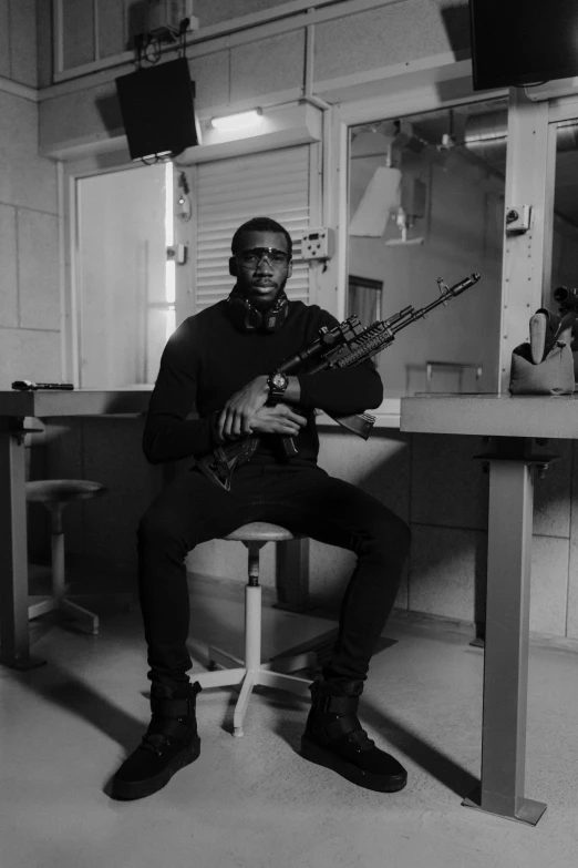 a man sitting on a stool holding a gun, a black and white photo, inspired by Theo Constanté, wakanda, in a classroom, heavily armed, mod