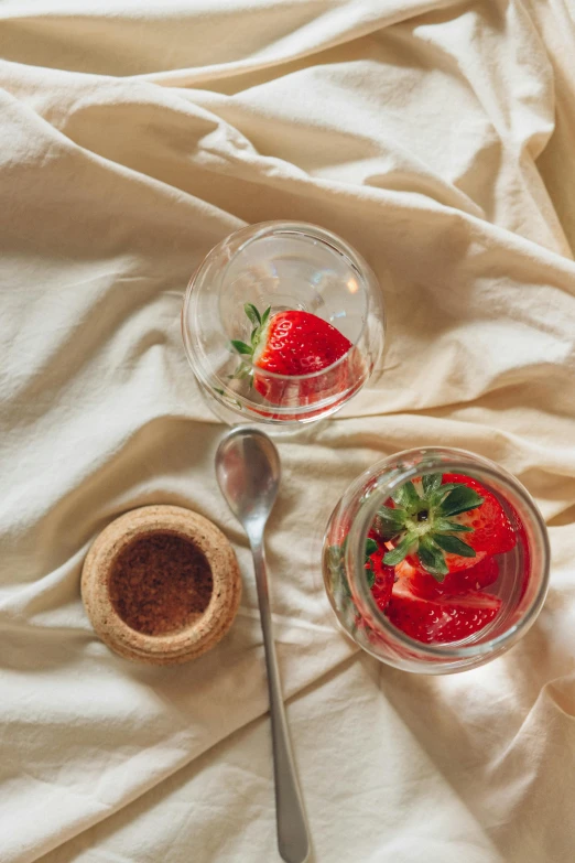 a couple of desserts sitting on top of a bed, a still life, unsplash, photorealism, strawberry, glass tableware, full frame image