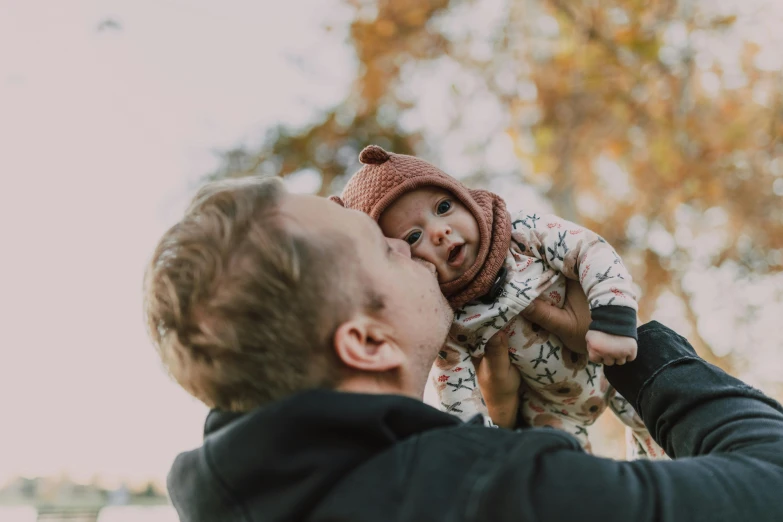 a man holding a baby up in the air, by Emma Andijewska, pexels contest winner, at a park, warm friendly face, manuka, 1 6 x 1 6