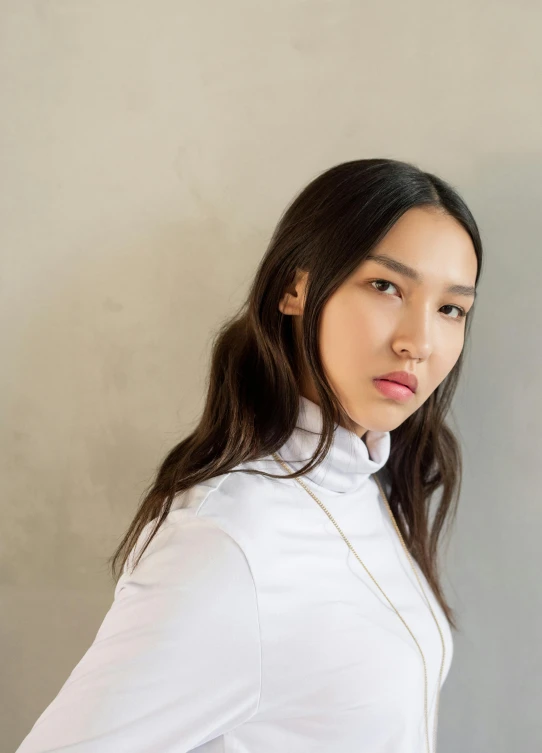a woman standing in front of a gray wall, an album cover, inspired by Kim Tschang Yeul, trending on unsplash, in white turtleneck shirt, dua lipa, headshot profile picture, wearing a white button up shirt