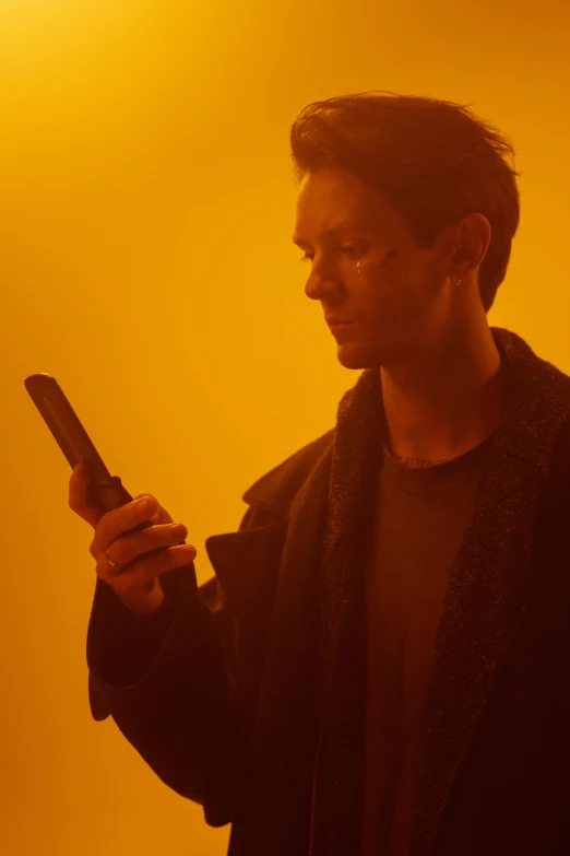a man holding a cell phone in his hand, an album cover, by Joseph Severn, pexels, bauhaus, yellow light, actor, intense atmospheric, 2 1 savage