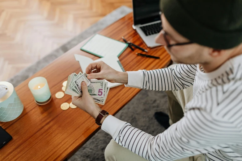 a man sitting at a table holding a stack of money, by Julia Pishtar, pexels contest winner, thumbnail, 🦩🪐🐞👩🏻🦳, sitting on a table, transforming