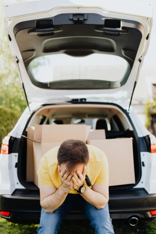 a man sitting on the ground in front of a car, a picture, shutterstock, renaissance, two exhausted, box, face down, at home