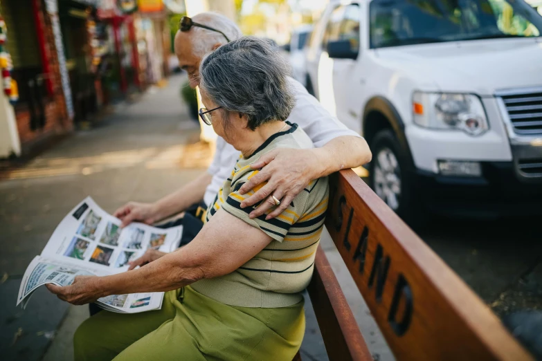 a couple of people that are sitting on a bench, a picture, unsplash, photorealism, reading a newspaper, hugging, older woman, a long-shot