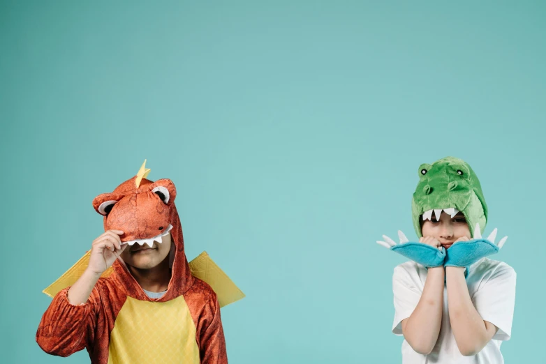 two children wearing dinosaur costumes standing next to each other, trending on pexels, hand over mouth, with a blue background, playing games, wearing a fancy dress