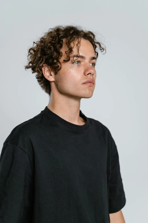 a young man with curly hair wearing a black t - shirt, trending on unsplash, black oversized clothes, head turned to the side, federation clothing, slightly tanned