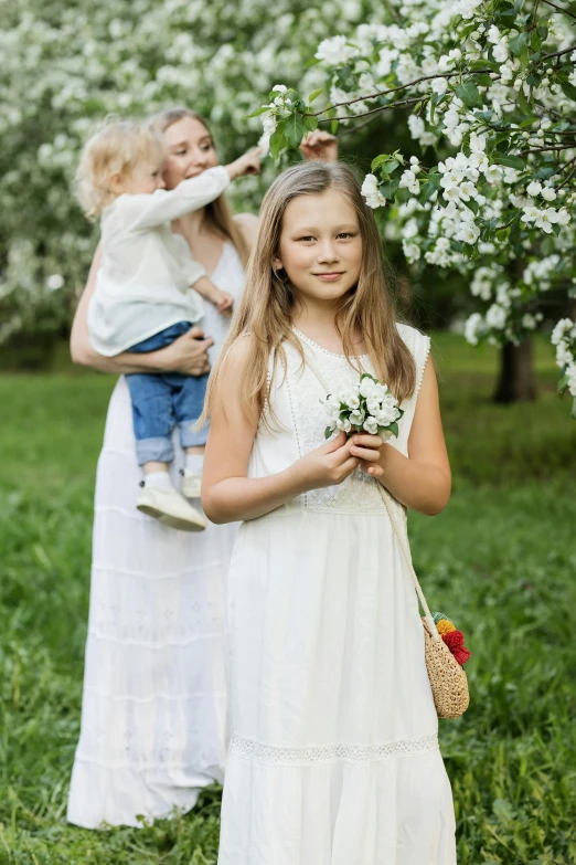 a woman holding a little girl in a white dress, inspired by Elsa Beskow, shutterstock, fruit trees, bouquets, celebration, denim