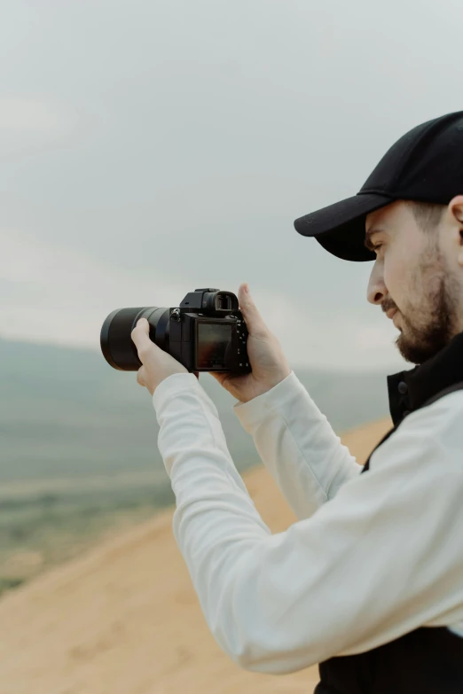 a man standing on top of a sandy beach holding a camera, professional profile picture, from 8 k matte, a wanderer on a mountain, zoomed in