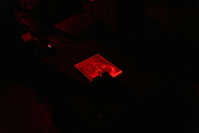 a laptop computer sitting on top of a table in a dark room, holography, red monochrome, sitting on a lab table, seen from above, light casting onto the ground